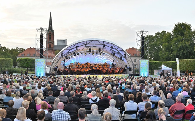 Open-Air-Bühne mit großem Orchester und tausenden Zuschauern im Vordergrund